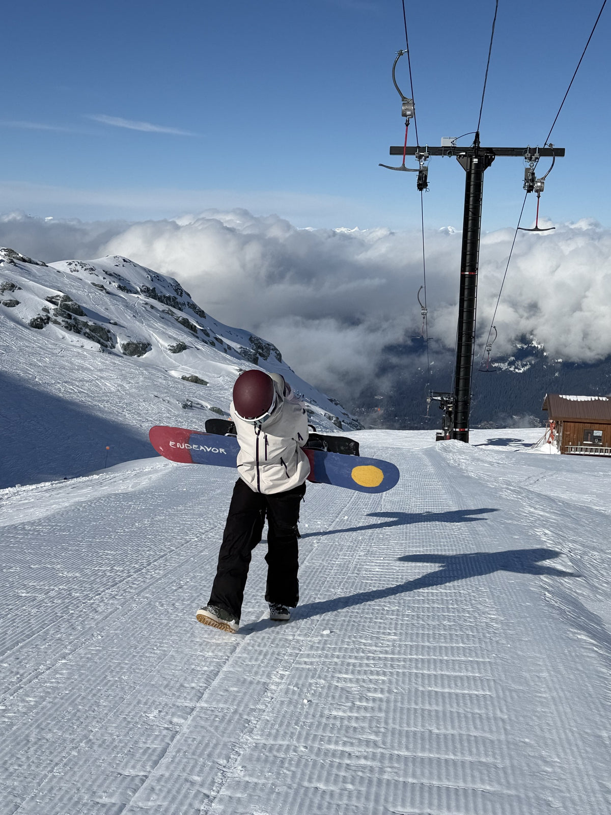 Rider hiking up a groomed run under the chairlift, carrying her snowboard