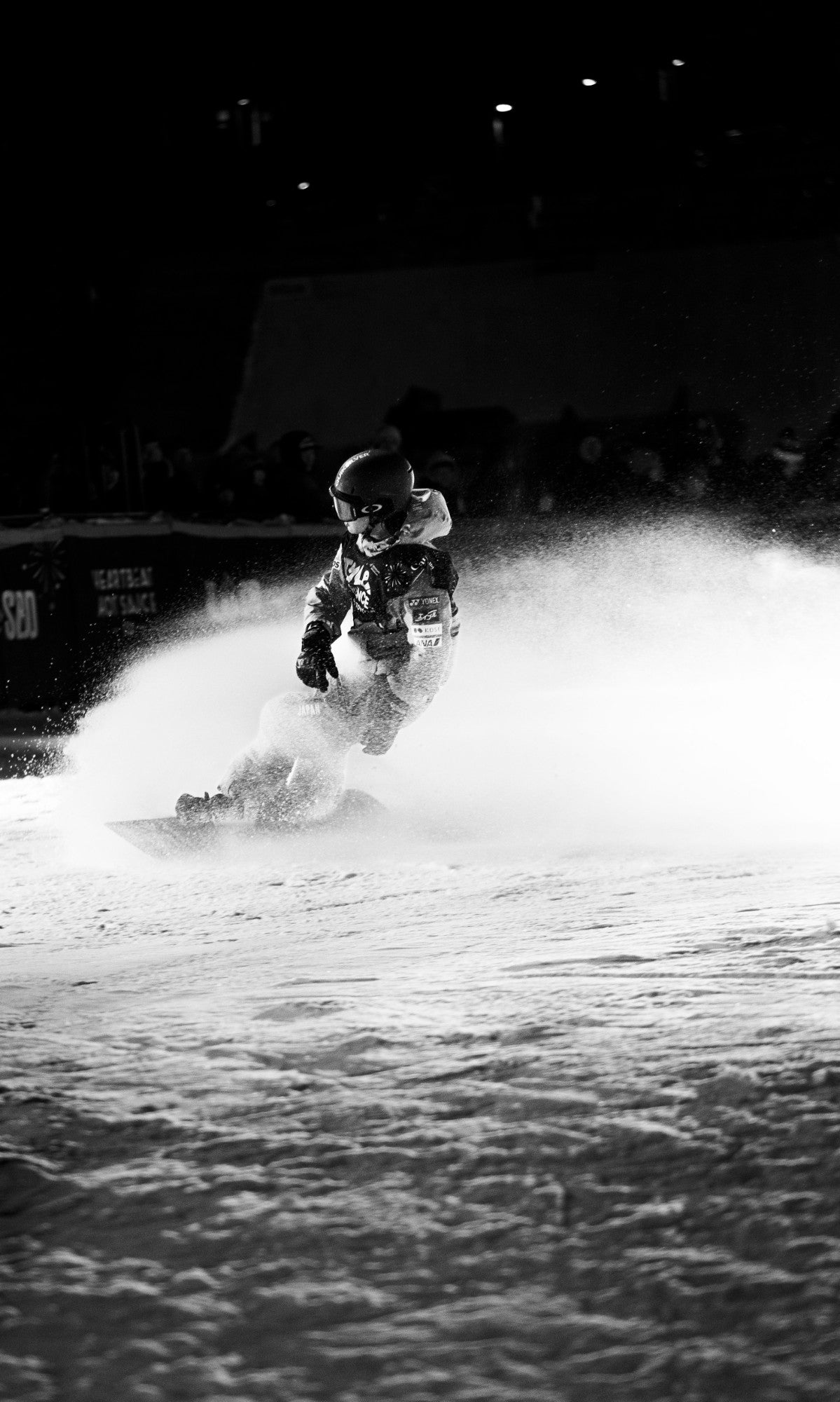 Snowboarder carving through spray under the lights at night