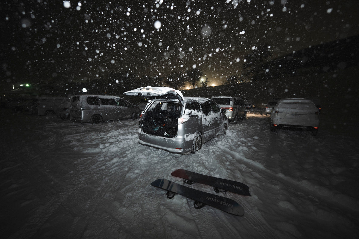 Two Endeavor snowboards in a snowy car park at night, heavy snowfall