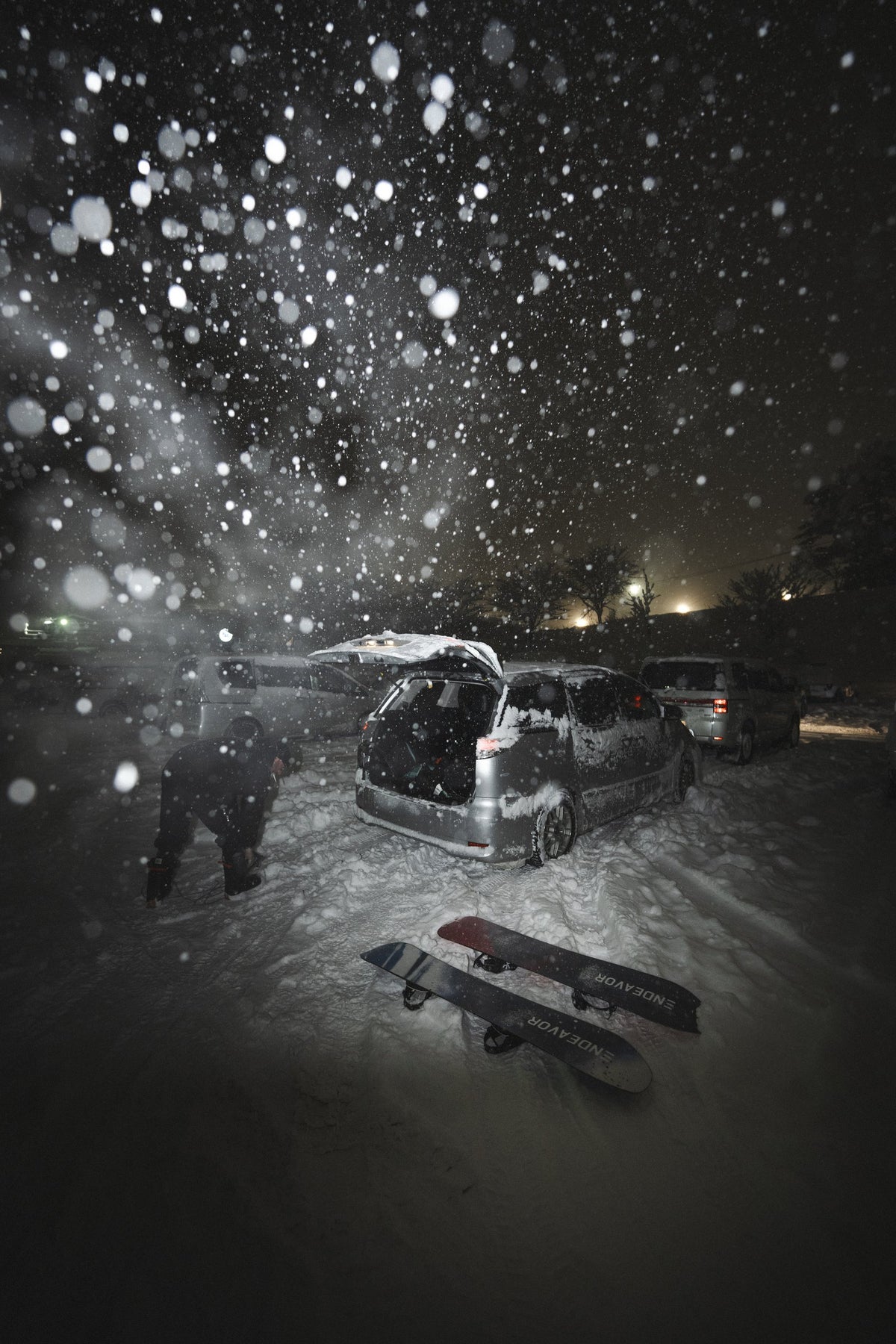 Snowboards in a snowy car park at night, storm coming down