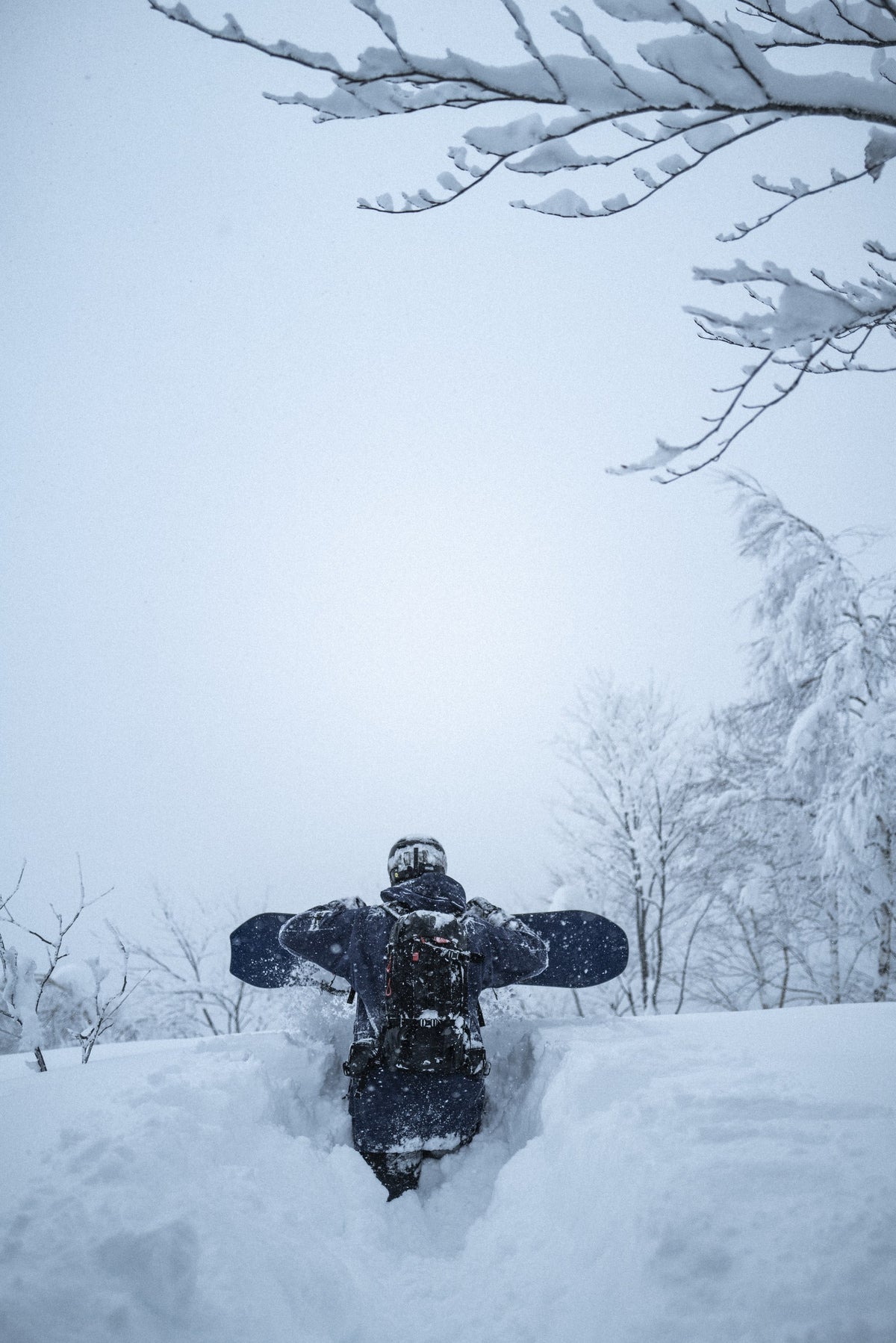 Snowboarder hiking through deep powder with a board on his pack