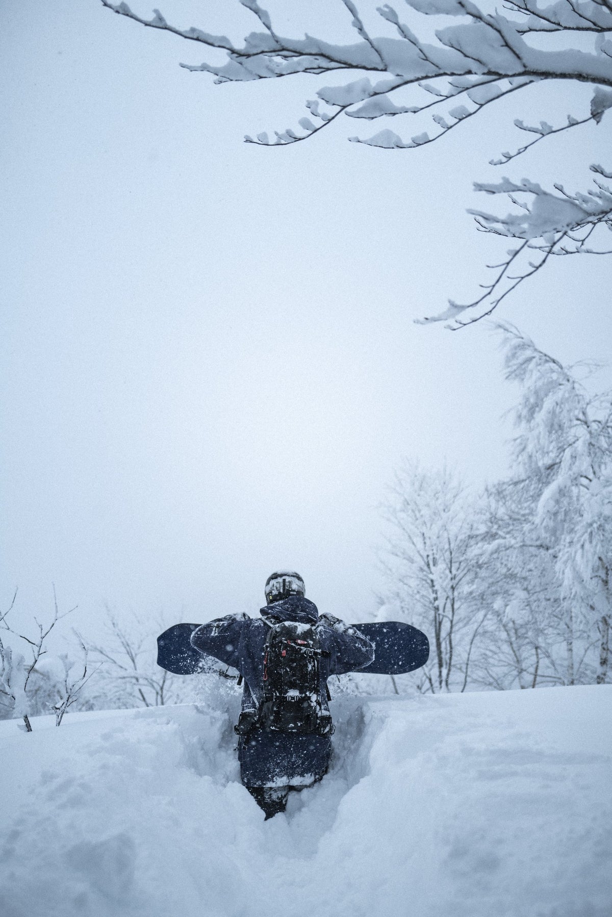 Rider in deep snow with the Endeavor Scout Pro snowboard across the shoulders, Japan