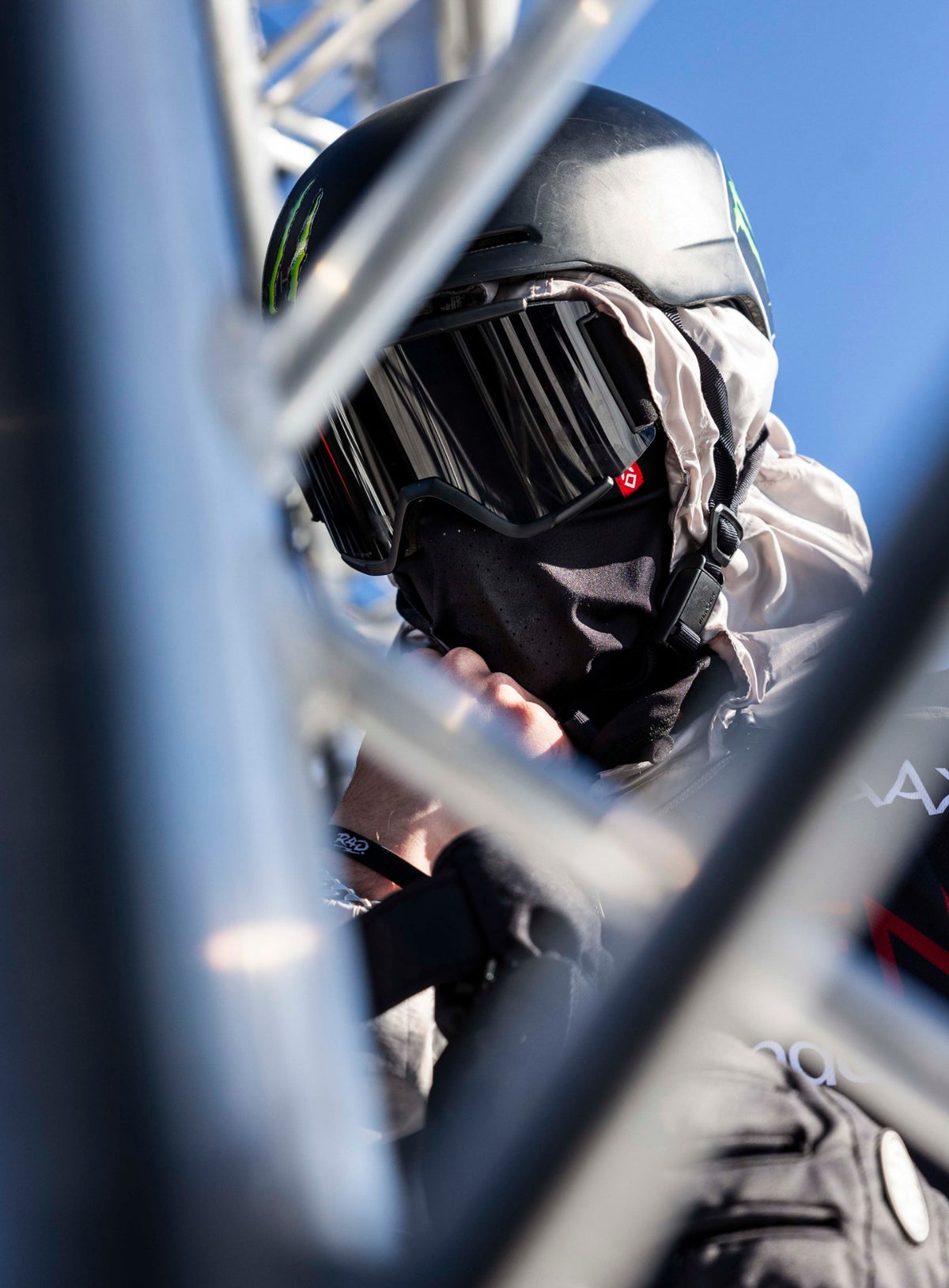 Rider in a black Airhole laser balaclava, helmet and goggles, framed by start-gate scaffolding