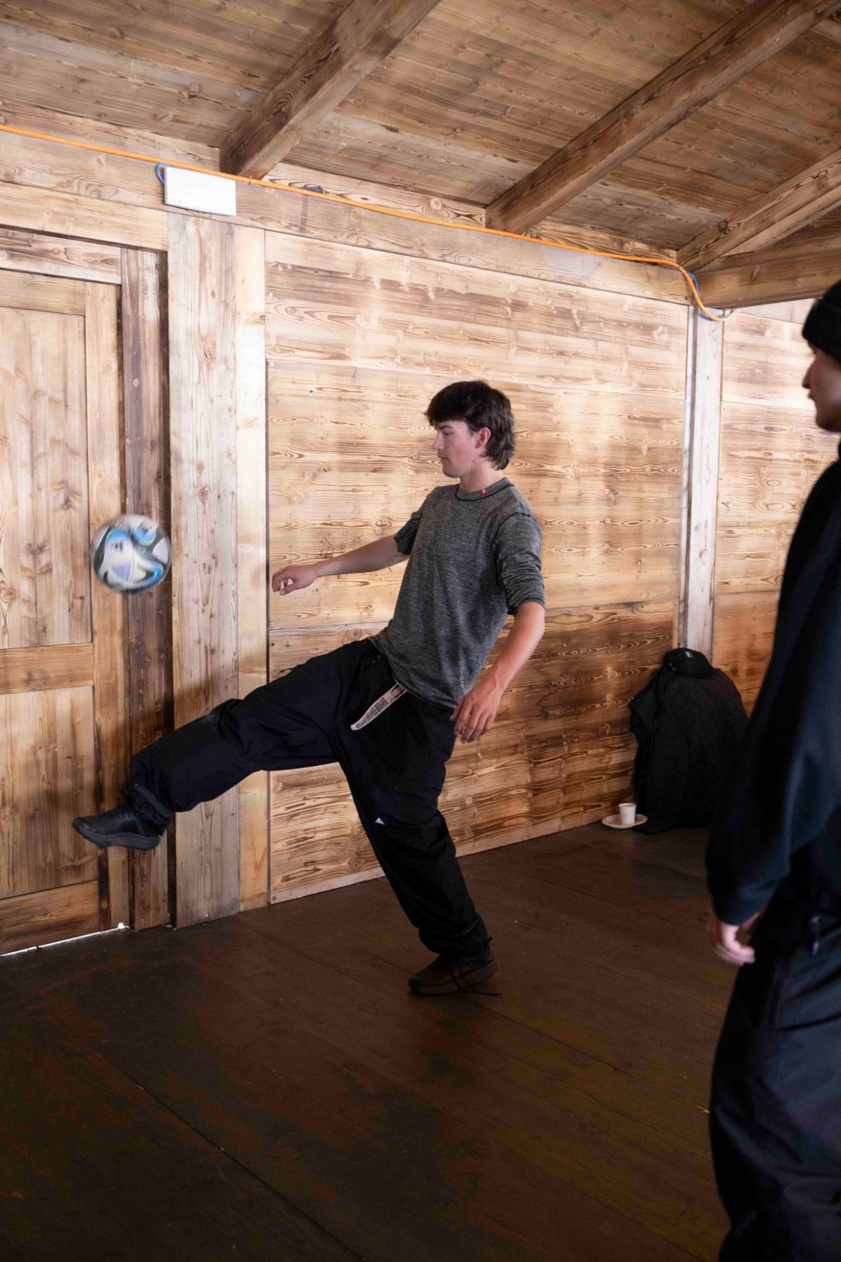 Rider in an Airhole thermal top juggling a football in a wooden mountain hut