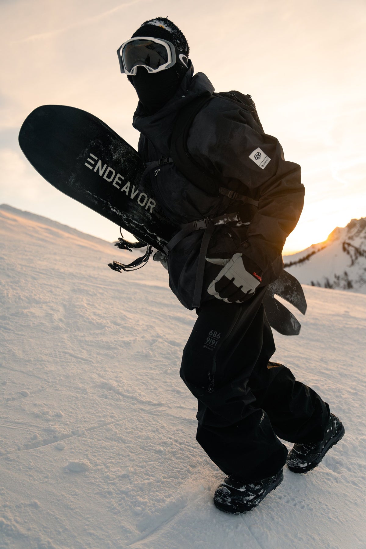 Rider carrying an Endeavor snowboard at sunset