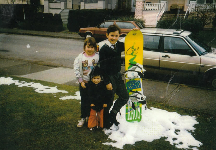 Kids with a snowboard on a front lawn with patches of snow