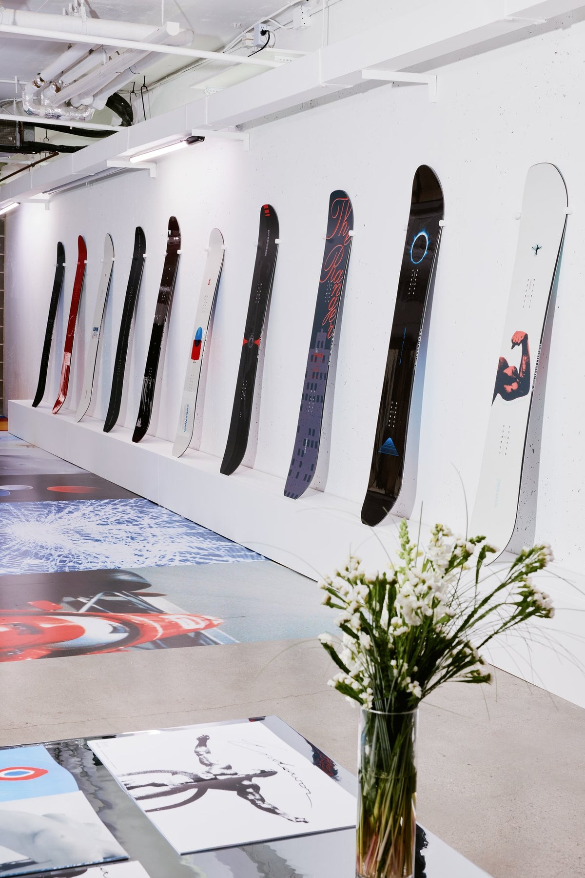 The wall in perspective: Maks Eidelson's board graphics on a white ledge, prints on the floor, white flowers on a mirrored table